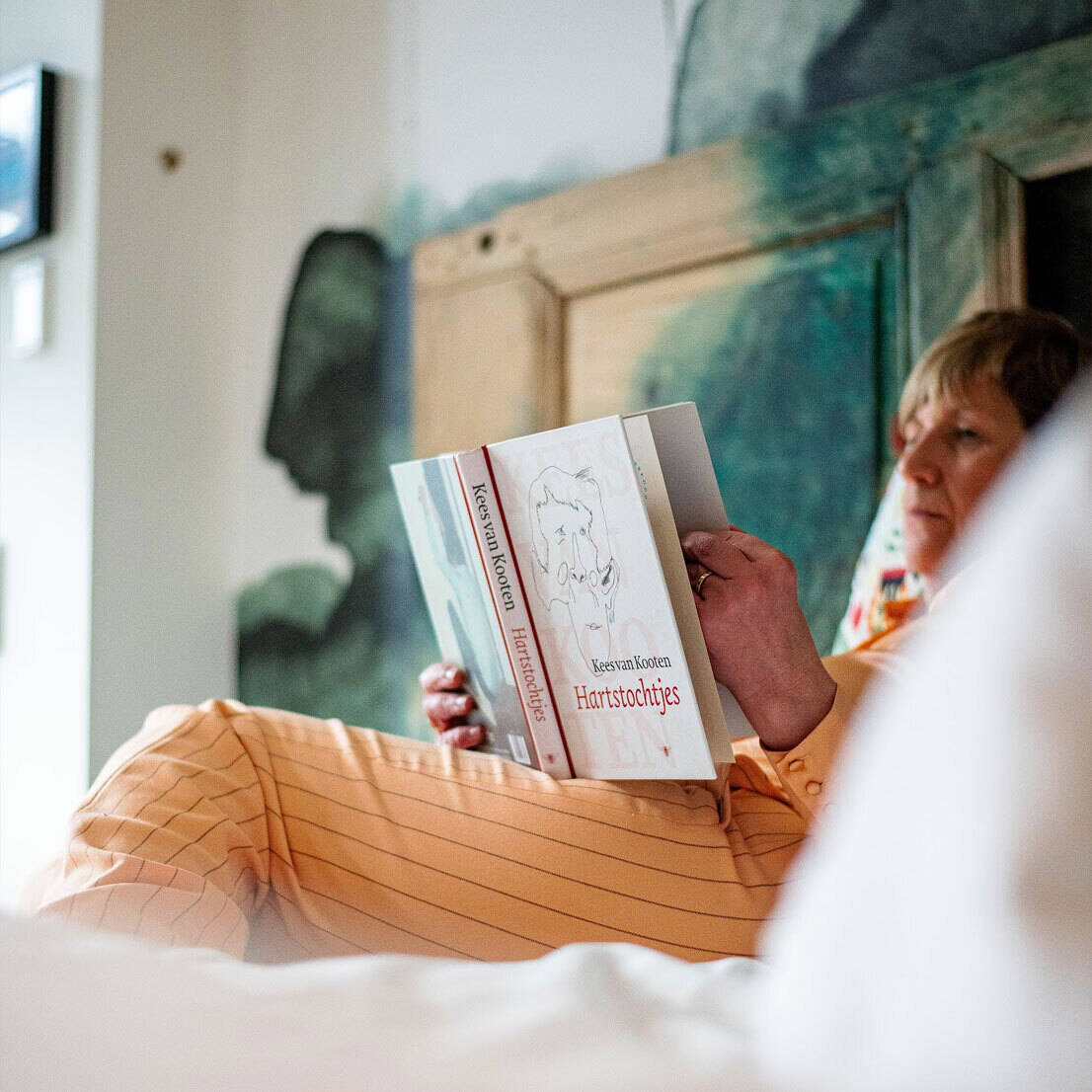 Guest reads relaxed in an artistically furnished hotel room with watercolour wall.