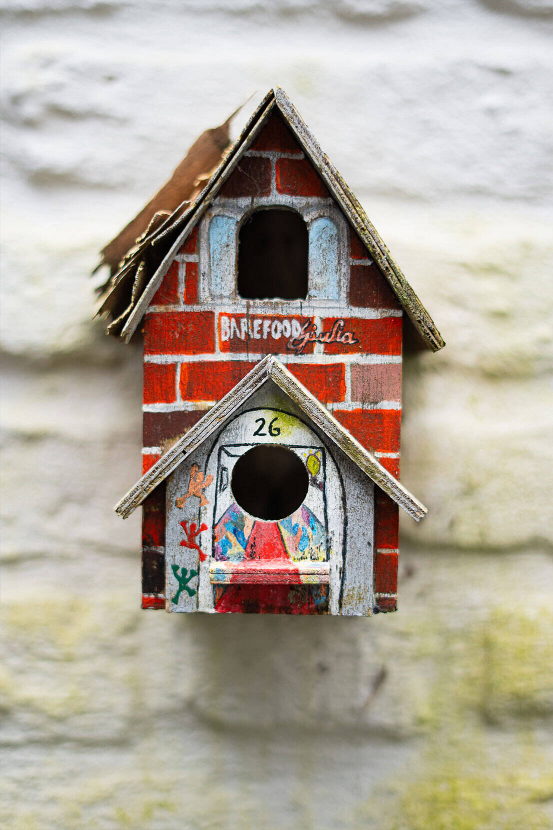 Handgefertigtes Vogelhäuschen mit BareFoodGiulia-Logo an weißer Wand - Symbol des Heimkommens mit Charakter