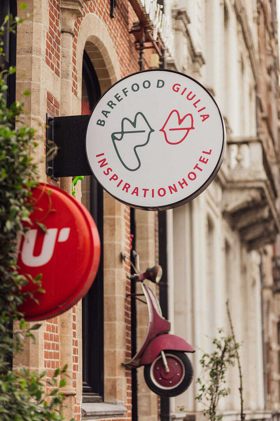 Enseigne de l'hôtel BareFoodGiulia Inspirationhotel avec visages stylisés et décoration Vespa rouge sur la façade d’une maison de maître.